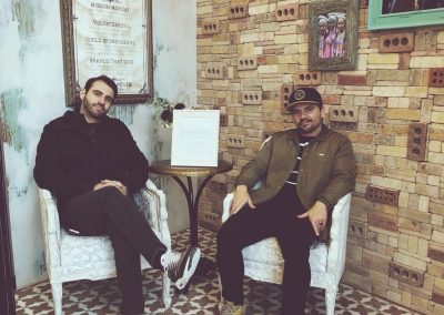 Jake Kramer sits beneath a Give Back mission board in a brick-walled shop with a friend.
